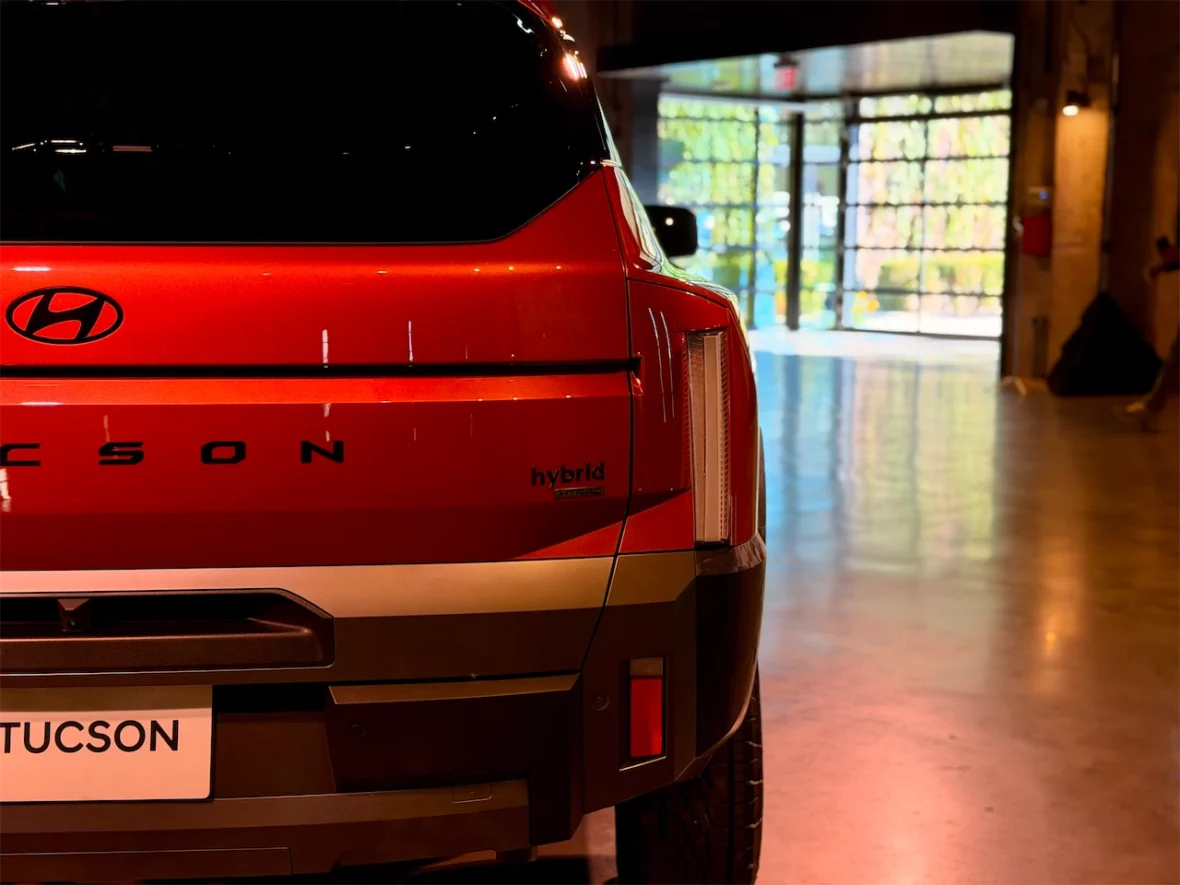 Rear view of a red Hyundai Tucson hybrid SUV, showcasing the logo and model name on the tailgate in a well-lit indoor setting.