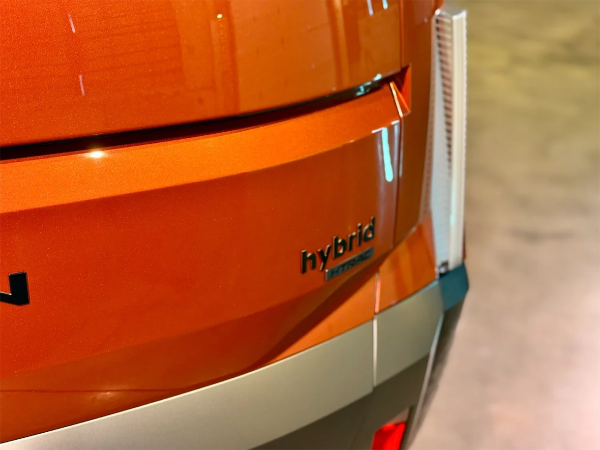 Close-up of the rear of a hybrid vehicle with an orange metallic finish, displaying the 'hybrid' badge.