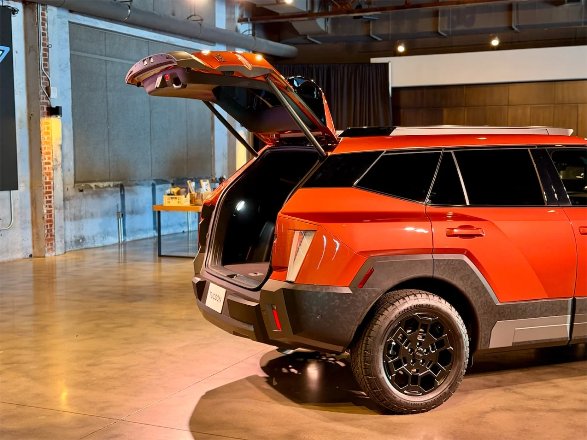 A red SUV with its rear hatch open, showcasing the spacious trunk area. The vehicle is displayed in a modern indoor setting with polished concrete floors and a stylish backdrop.