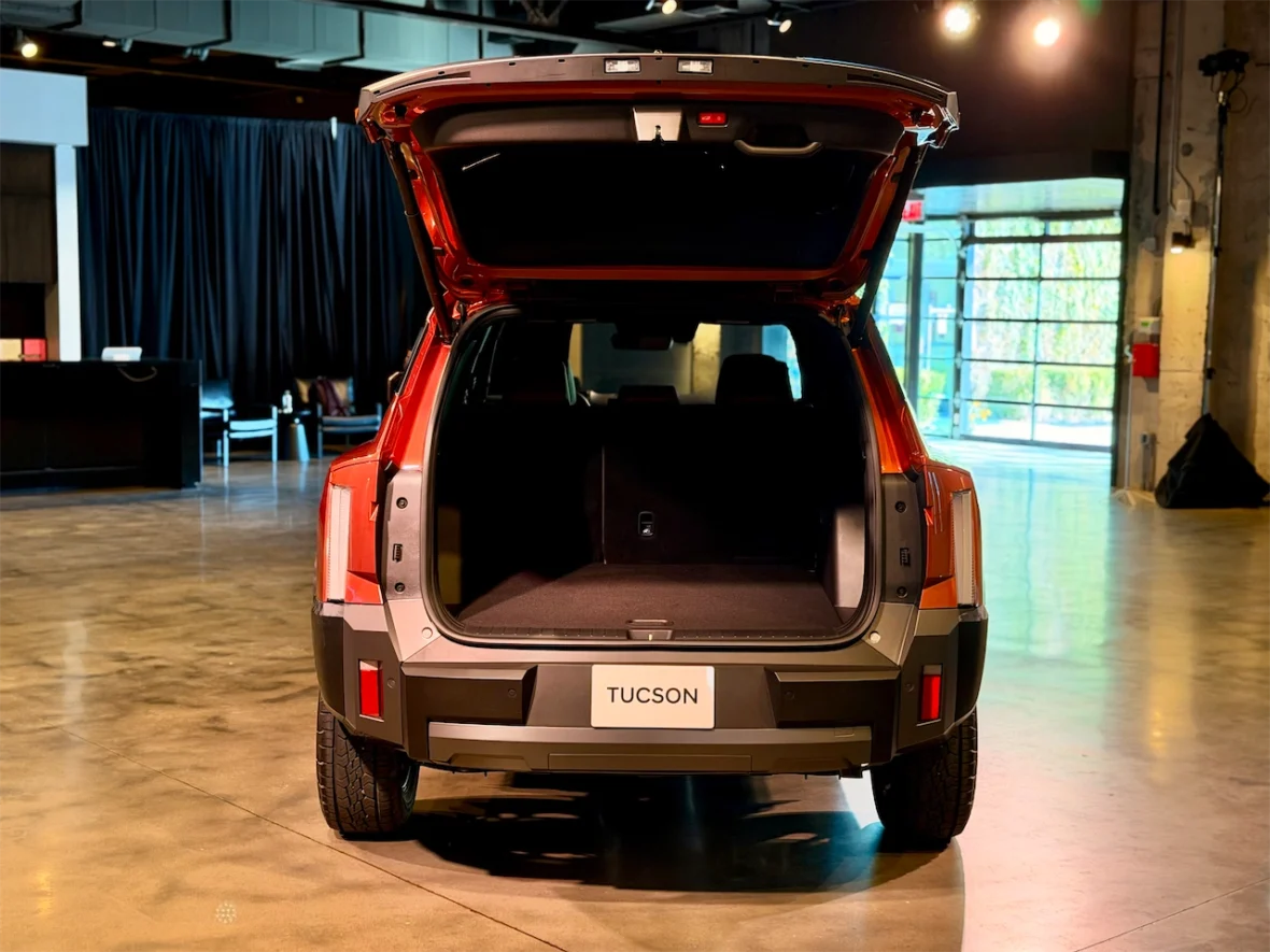 Rear view of an orange SUV with the trunk open, showcasing the spacious interior, in a well-lit modern showroom setting.