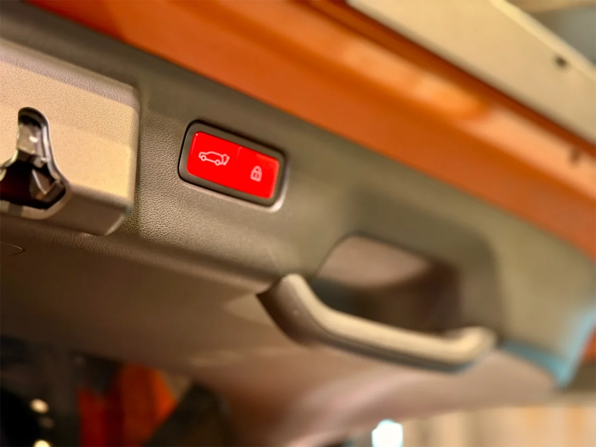 Close-up of a car's overhead control panel showing a red button with a car icon and a lock symbol, along with a keyhole for ignition.