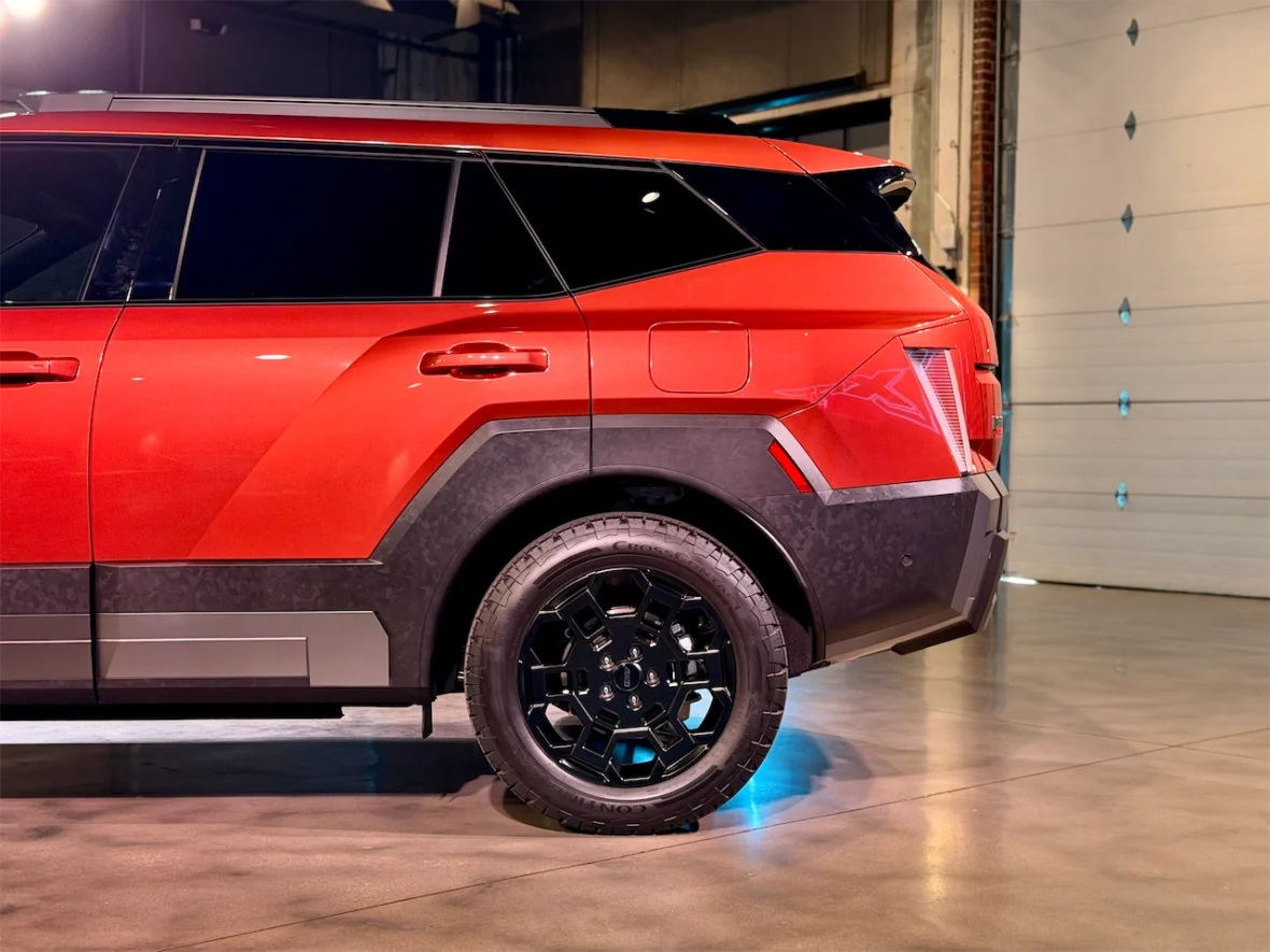 Side view of a red SUV showcasing its modern design and black wheel rims, set against a lit indoor backdrop.