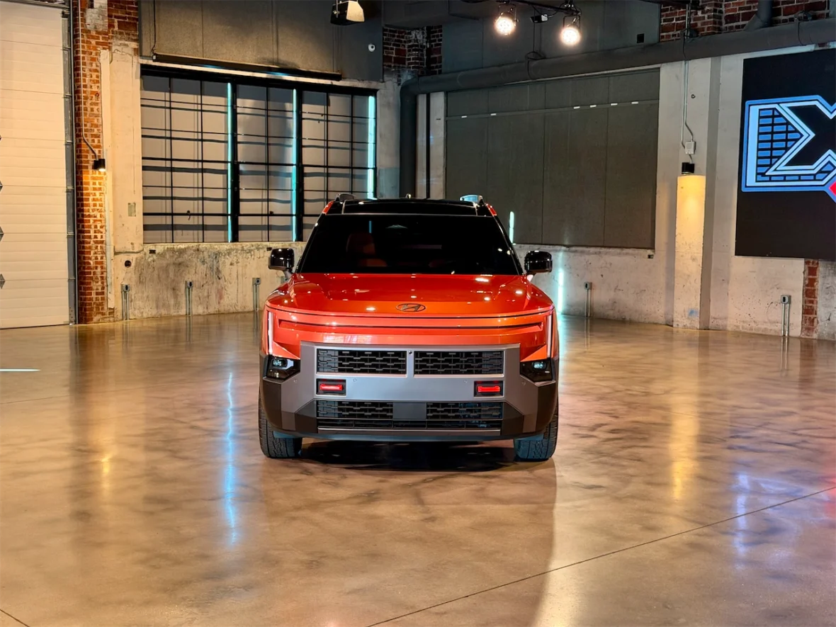 Front view of a modern electric vehicle displayed in an industrial setting with polished concrete flooring and large windows.