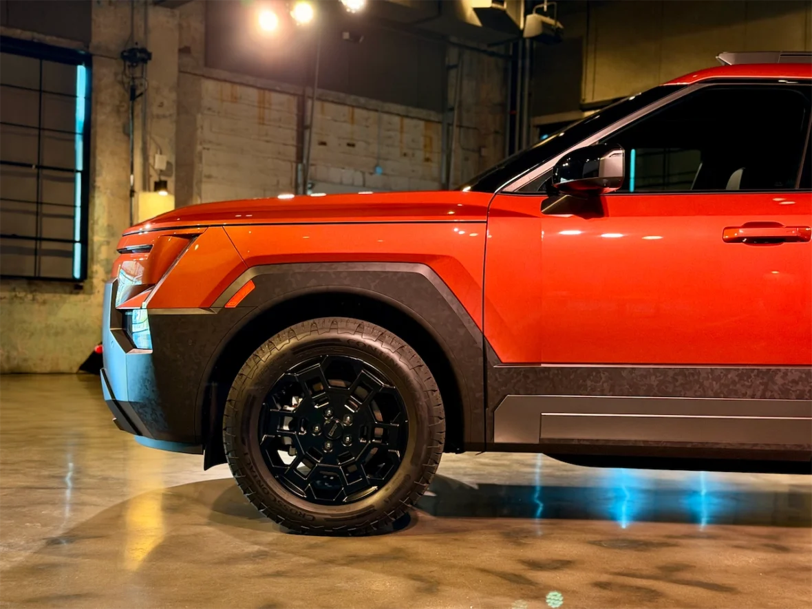 Side view of a red SUV with a black wheel and rugged tire in an industrial setting with dim lighting.