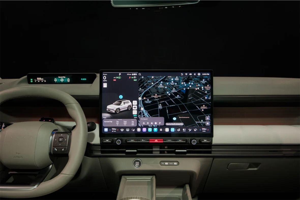 Interior view of a modern vehicle dashboard featuring a large touchscreen display with navigation maps and vehicle information, alongside a steering wheel and control buttons.