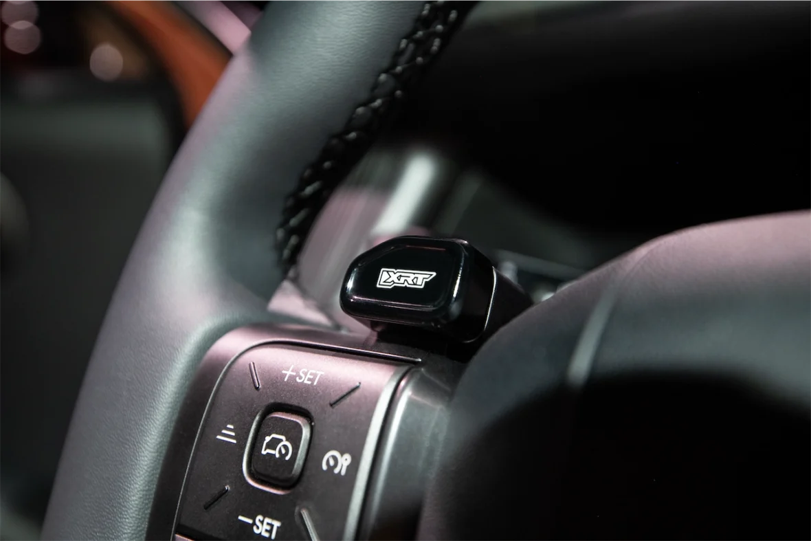 Close-up of a car steering wheel featuring a control button with the logo 'XRT' and surrounding controls.