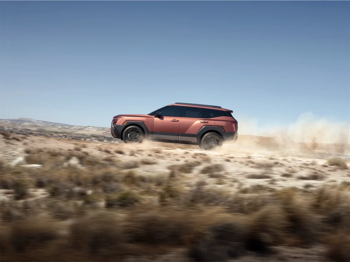 An off-road vehicle driving through a dusty landscape with mountains in the background.
