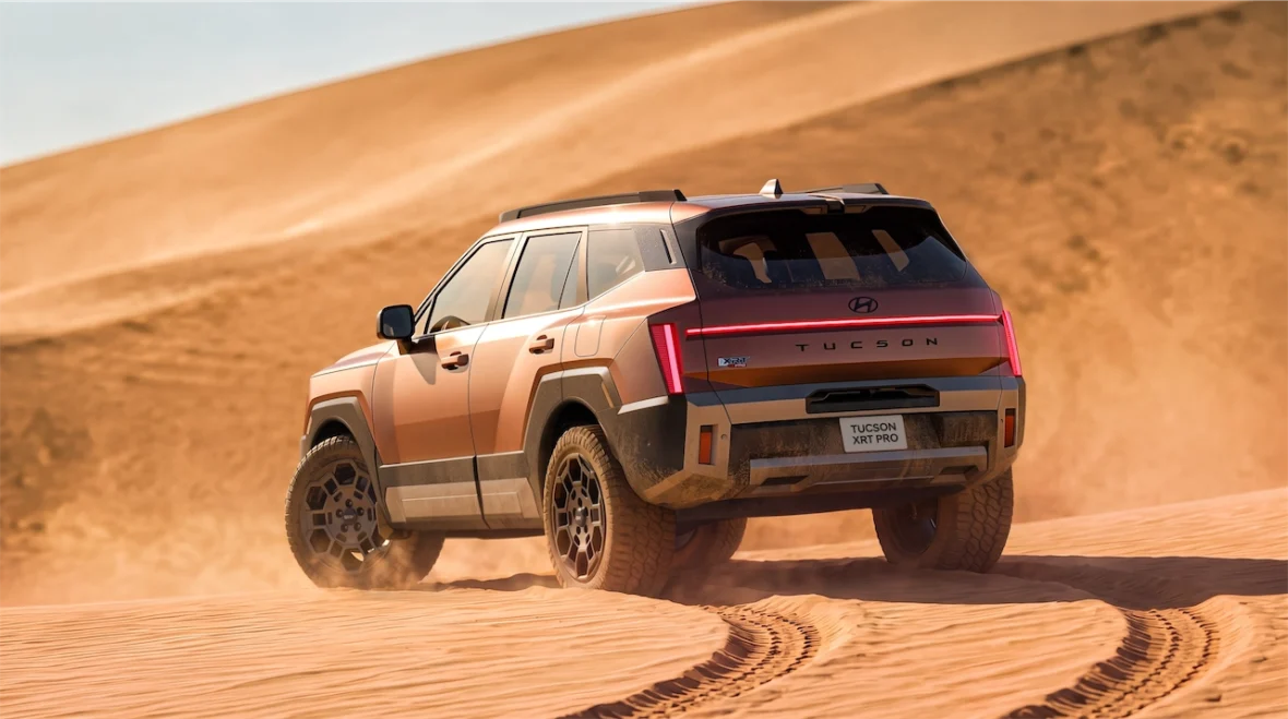 A Hyundai Tucson XRT Pro SUV driving through sandy terrain, kicking up dust in a desert landscape.