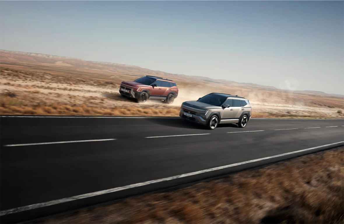 Two modern SUVs driving on a deserted road against a backdrop of mountains and clear skies.