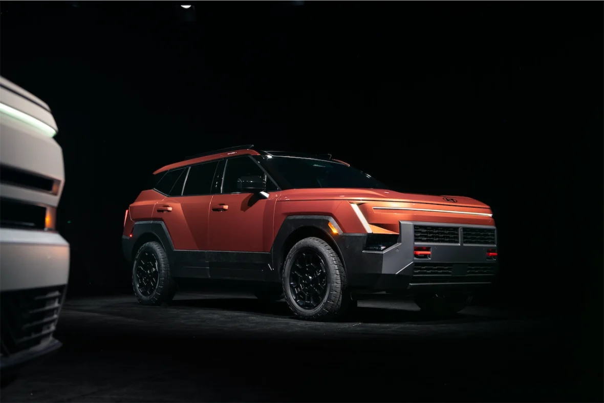 An orange SUV with a modern design, featuring black wheels and distinct geometric shapes, displayed in a dark setting.