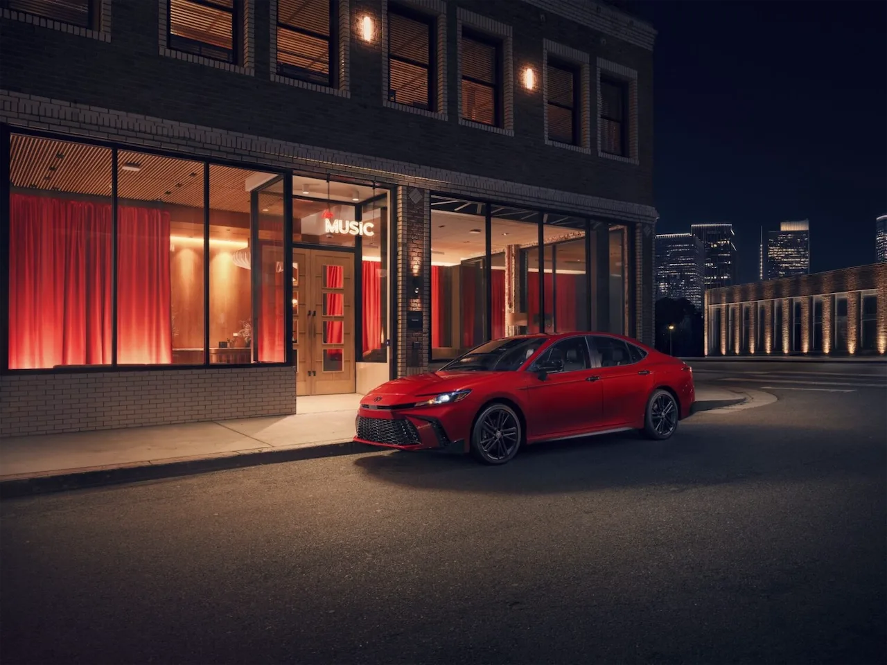 Red Toyota Camry Nightshade parked outside a lit building at night