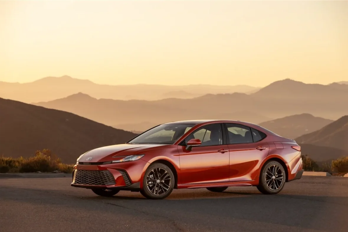 A red sedan car parked on a scenic road with mountains in the background during sunset.
