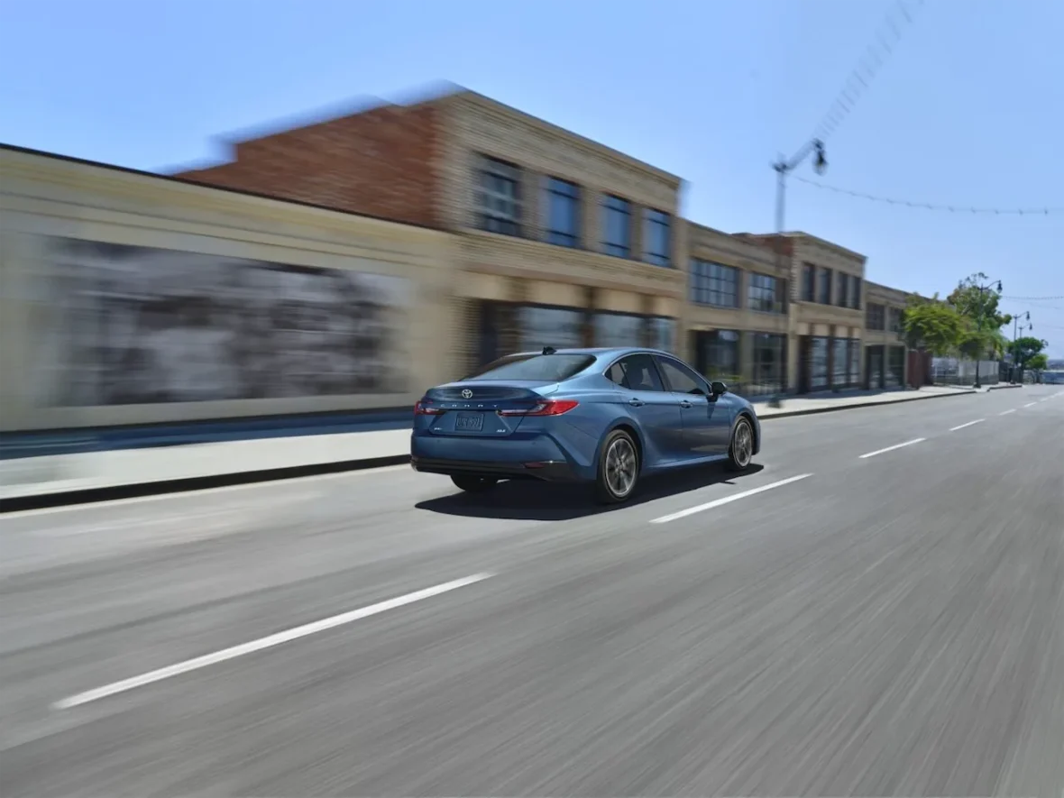 A blue car driving swiftly down a city street with blurred buildings in the background, indicating motion.