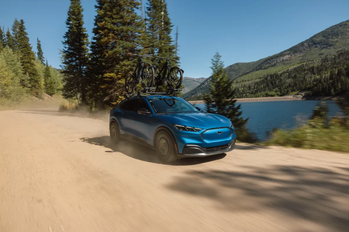 2027 Mustang Mach-E Trail driving on a gravel road beside a lake