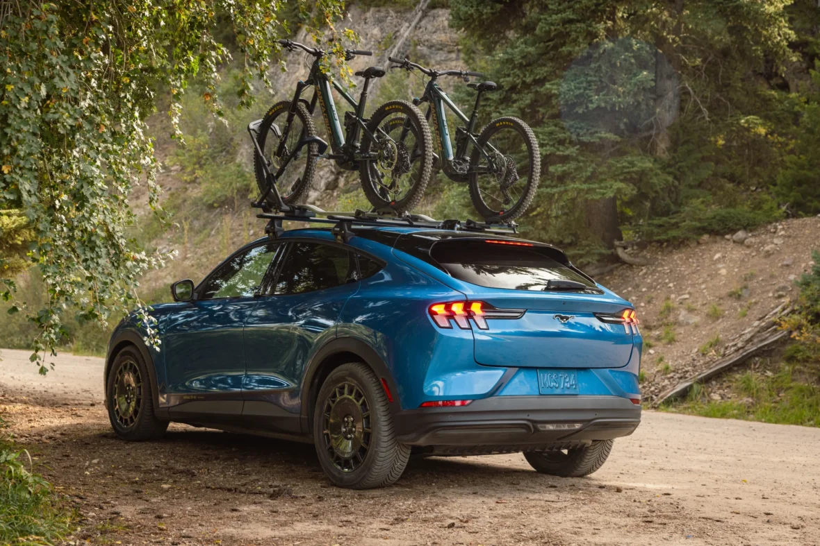 Rear view of an electric crossover with bikes on the roof on a dirt road