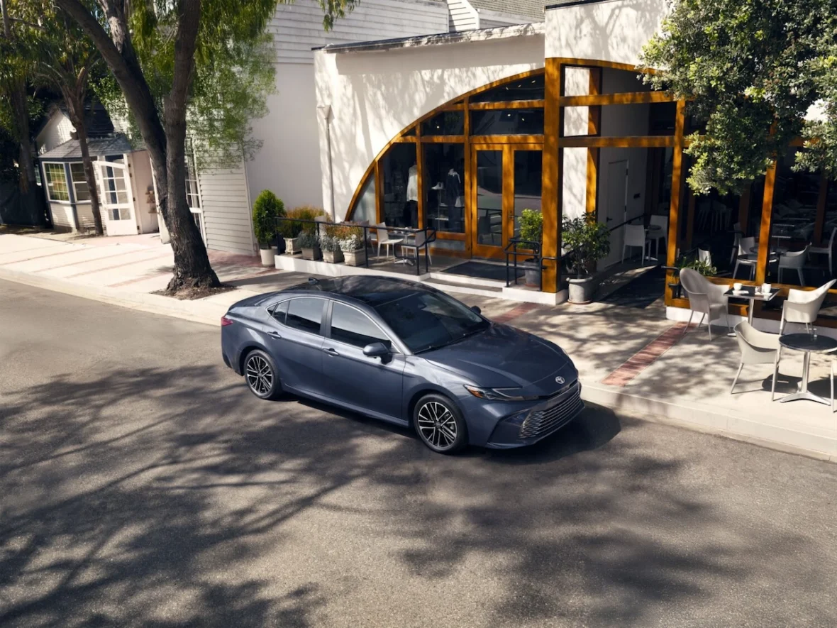 A sleek silver sedan parked near a modern restaurant with large windows and outdoor seating on a sunny day.