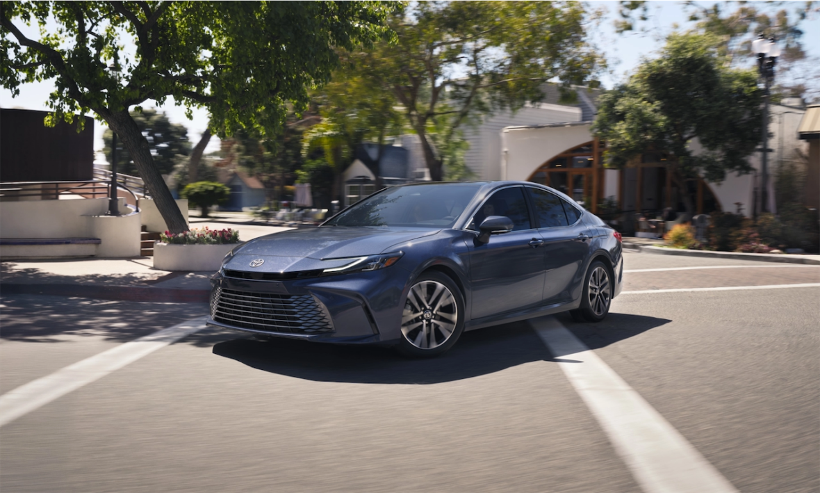 A sleek blue sedan turning left on a sunny street, surrounded by trees and buildings.