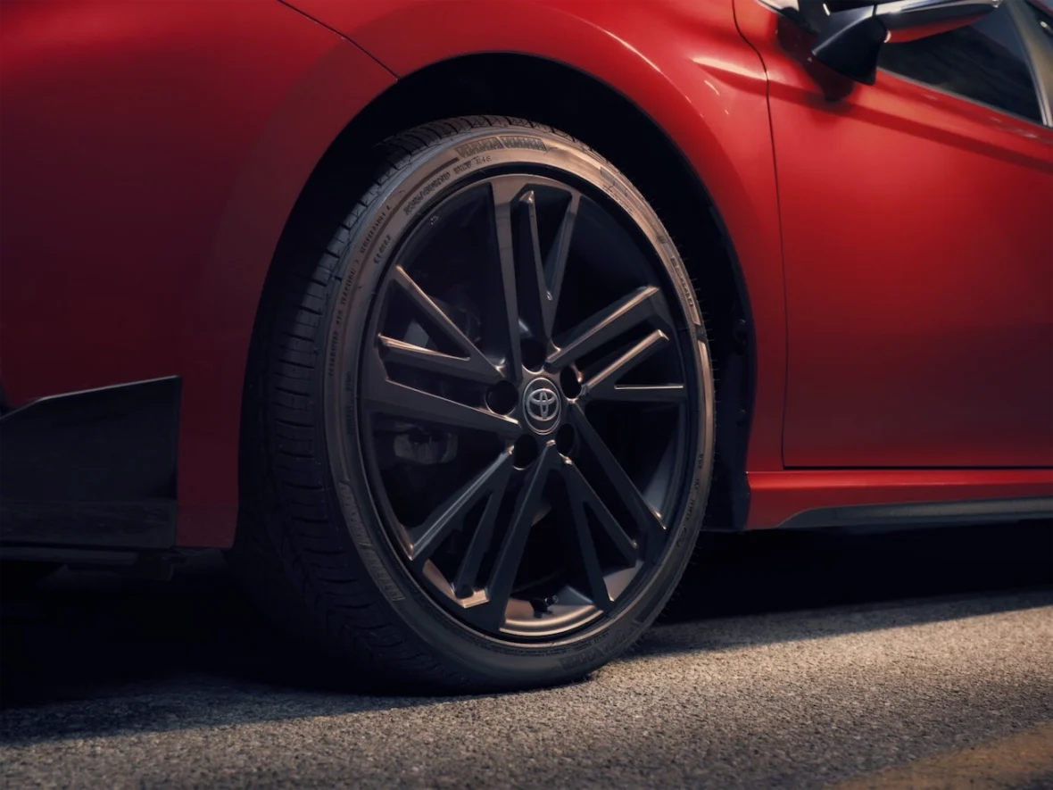 Close-up view of a black alloy wheel on a red car parked on asphalt.