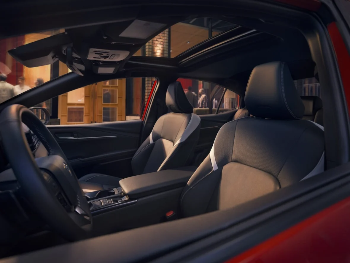 Interior view of a modern car showcasing dark leather seats and a panoramic sunroof, with a glimpse of an urban setting outside.