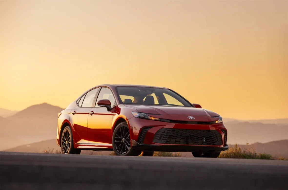 A red sedan parked on a scenic overlook during sunset, with mountains in the background.