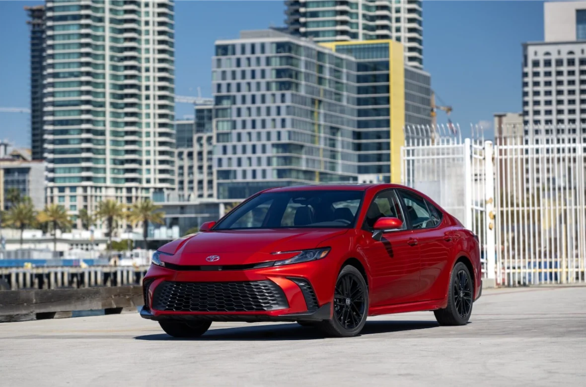 A red Toyota sedan parked in an urban setting, featuring modern high-rise buildings and palm trees in the background.