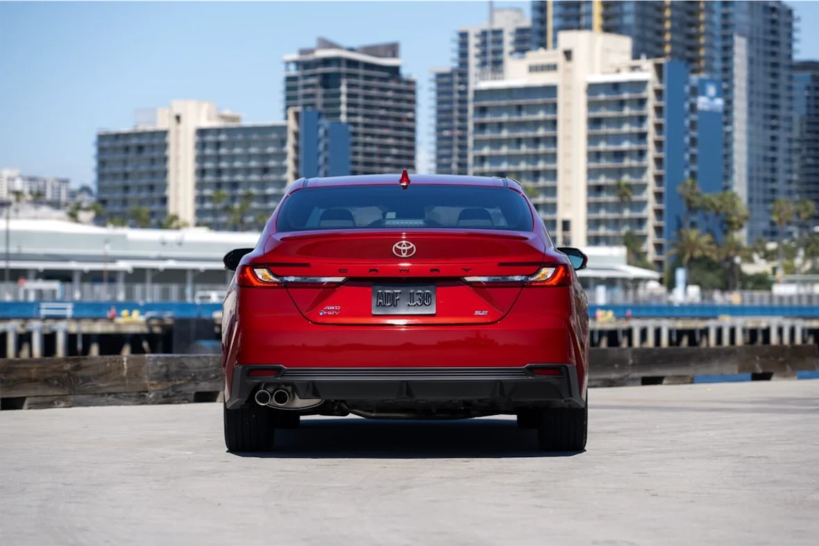 Rear view of a red Toyota Camry parked near a waterfront with tall buildings in the background.