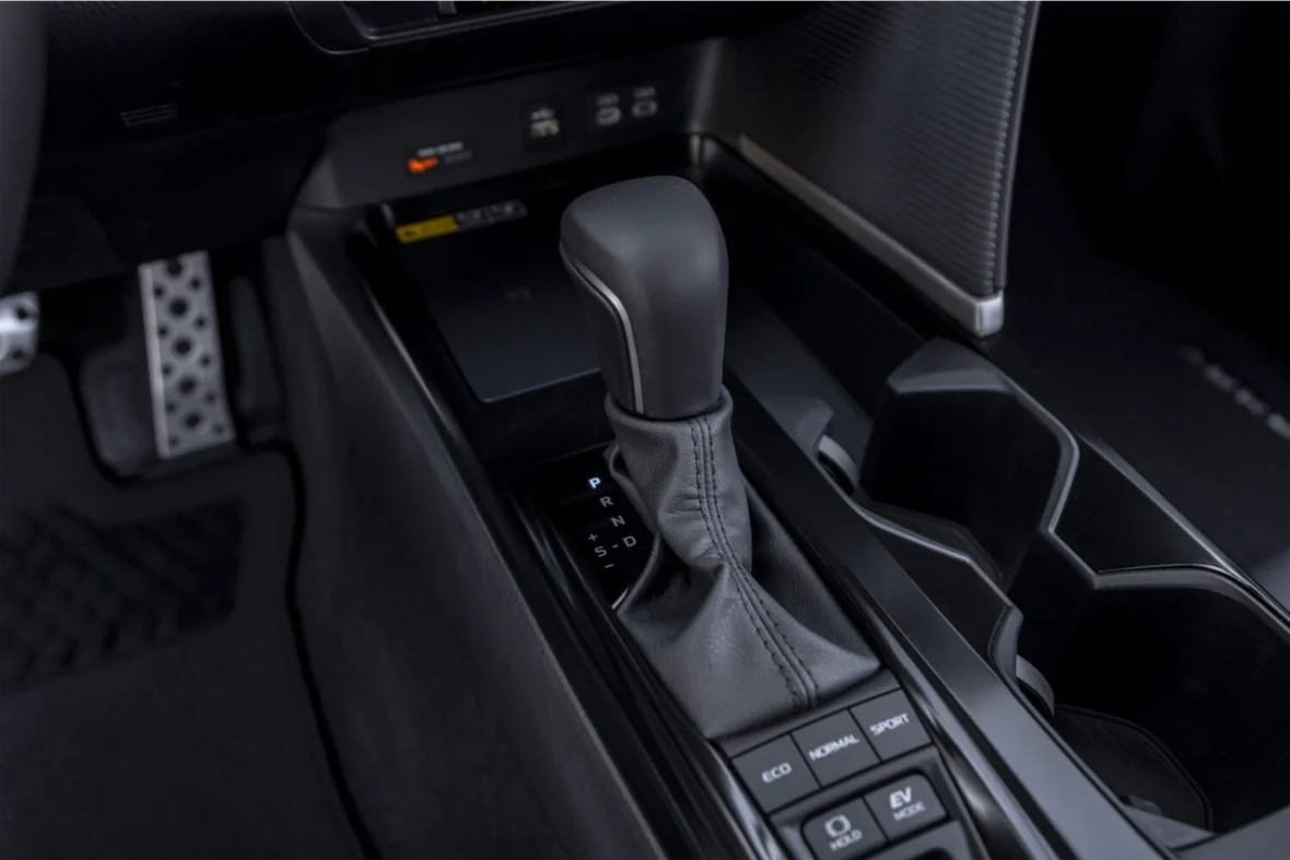Close-up view of a car's gear shift lever with a leather boot, featuring buttons for driving modes and cup holders in the console.