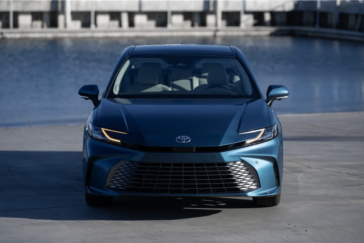 Front view of a blue Toyota car parked near a body of water with concrete structures in the background.