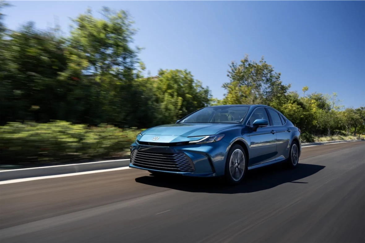 A blue sedan car driving on a road surrounded by greenery.