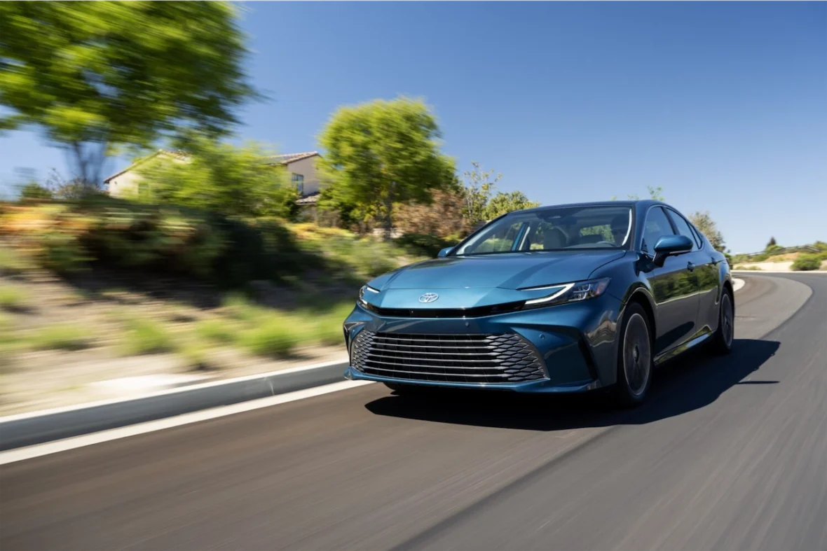 A blue Toyota sedan driving on a curvy road surrounded by greenery.