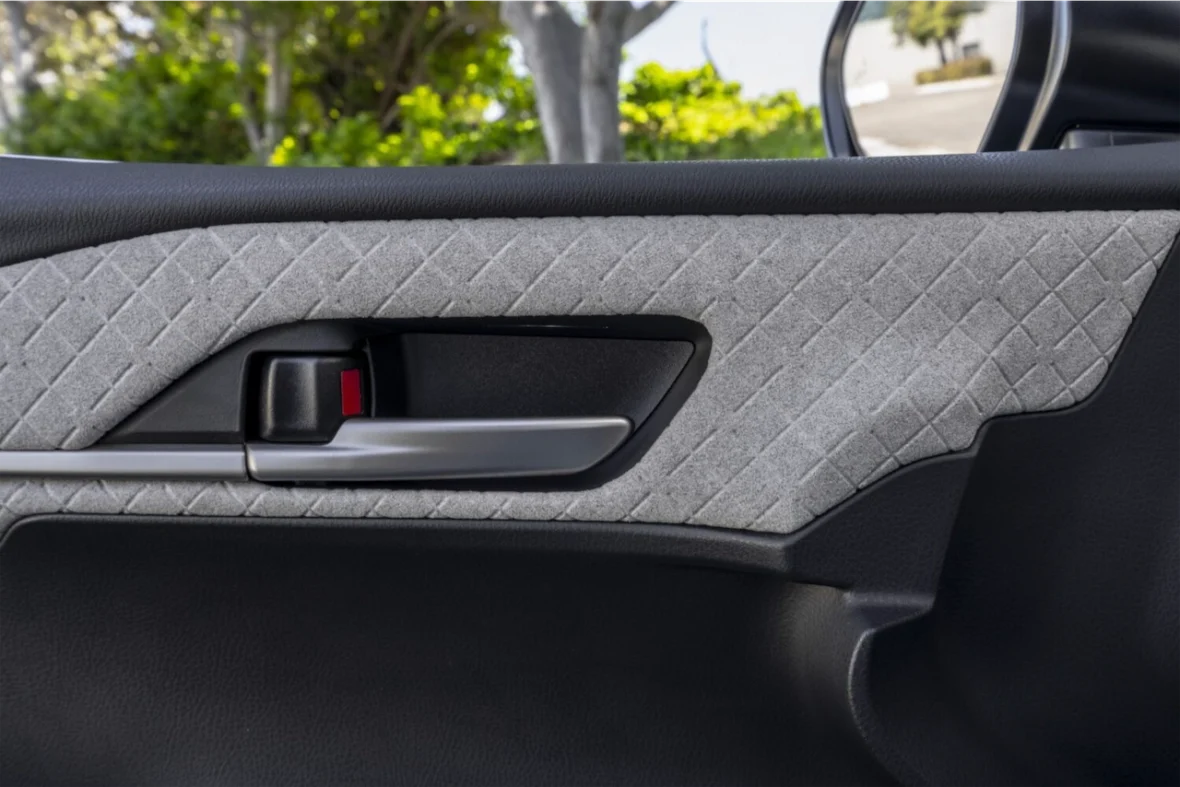 Close-up of a car door panel featuring textured gray fabric and a door handle with a chrome finish.