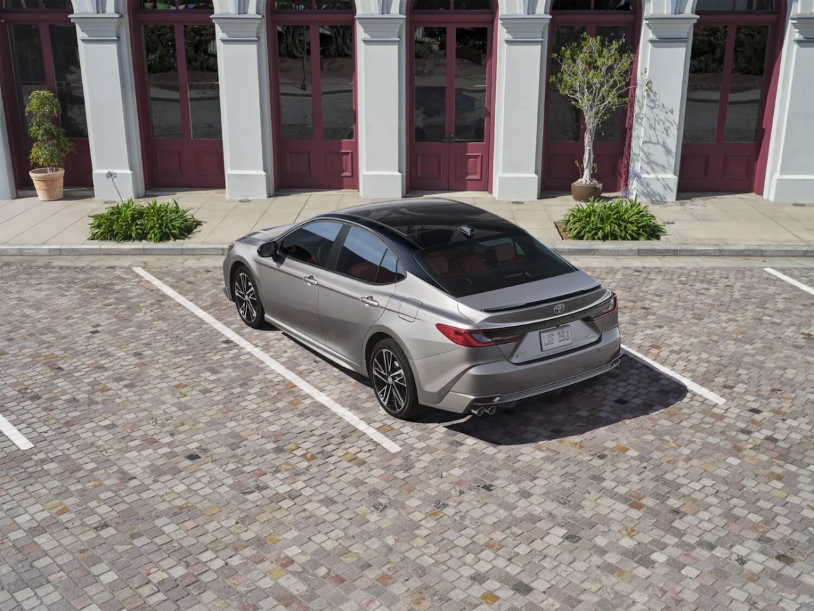 A silver sedan parked in a cobblestone lot, with a stylish design and a view of nearby lush greenery and historic architecture.