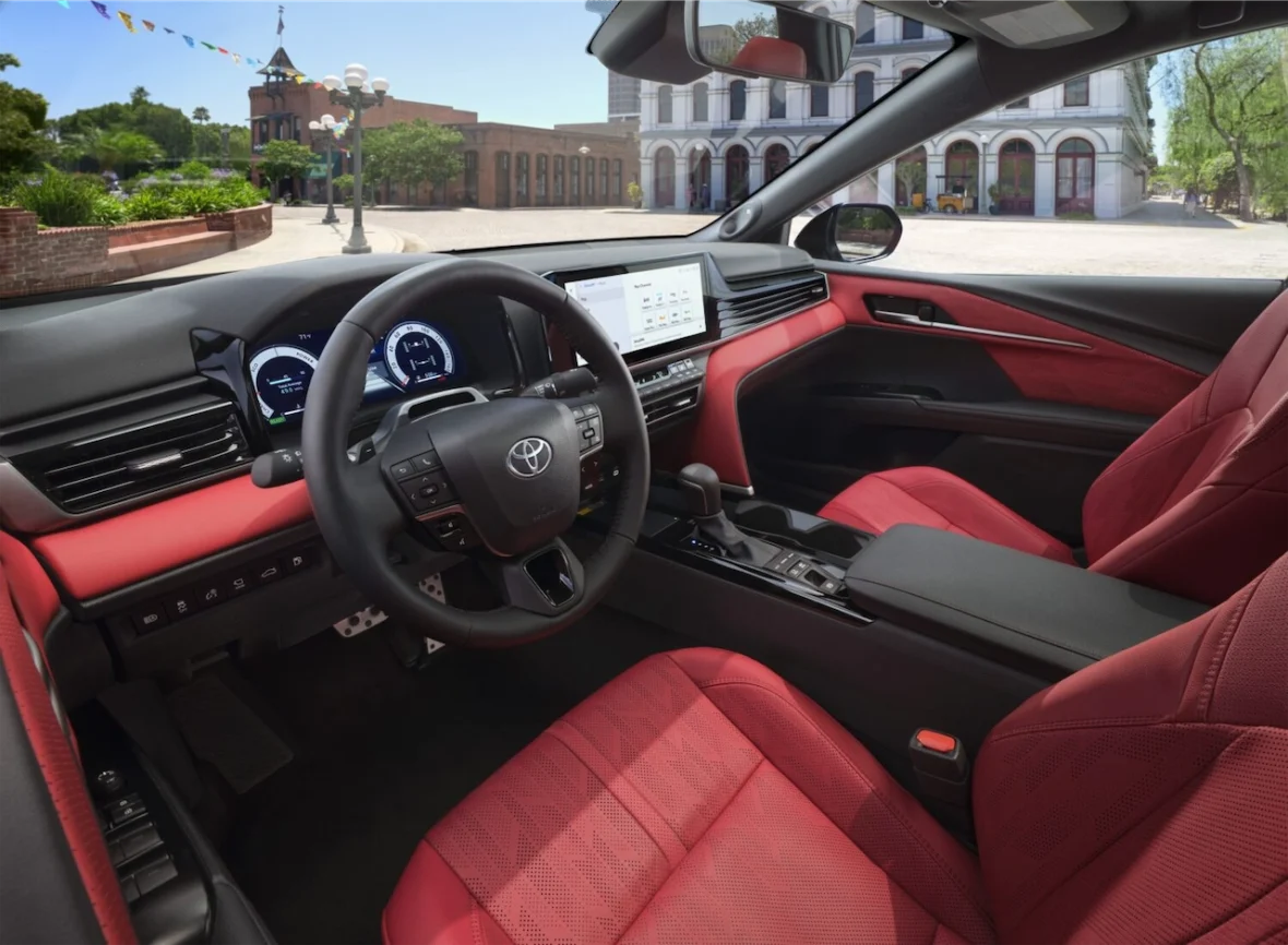 Interior view of a modern Toyota vehicle, featuring red and black upholstery, a sleek dashboard with a digital display, and a steering wheel with buttons.