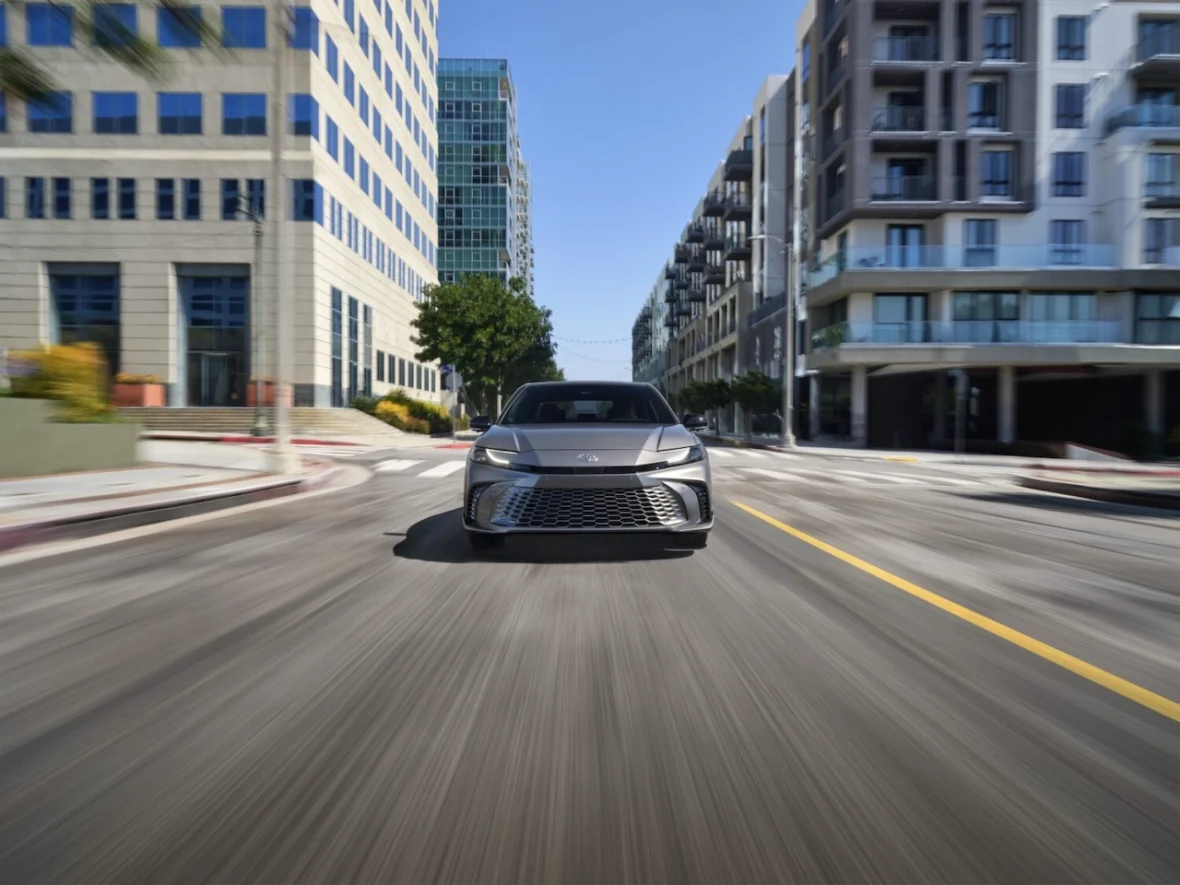Front view of a sleek car driving through a modern urban street with tall buildings on either side.