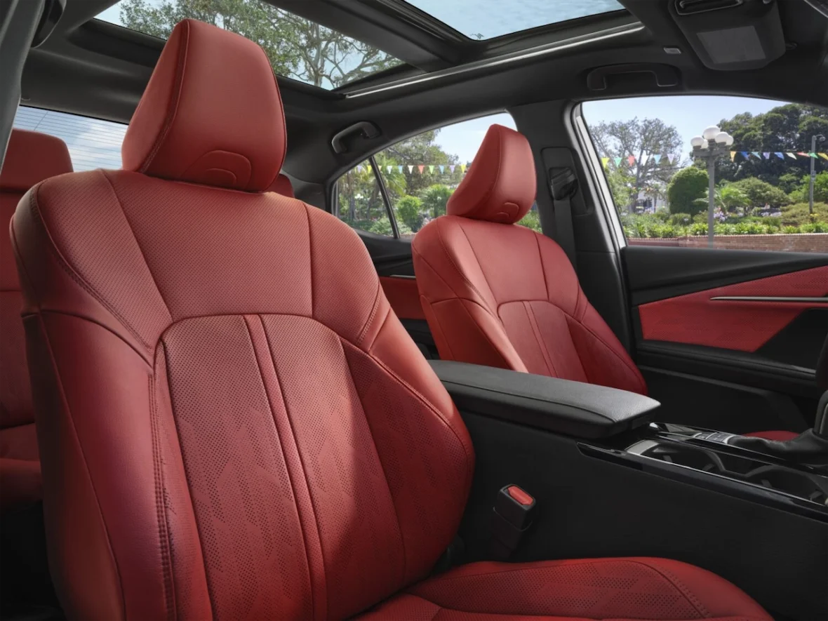 Interior view of a car featuring red leather seats and a sunroof, with a glimpse of greenery outside.