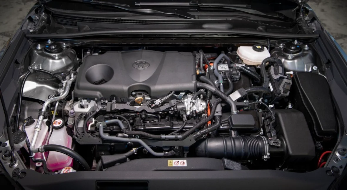 Close-up view of a Toyota engine compartment featuring various components such as hoses, the engine block, and a battery.