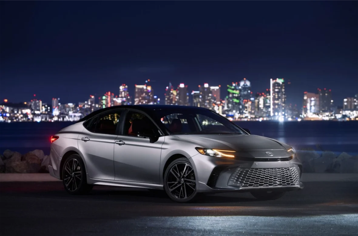 A silver sedan parked at night with a city skyline in the background, showcasing its sleek design and modern features.