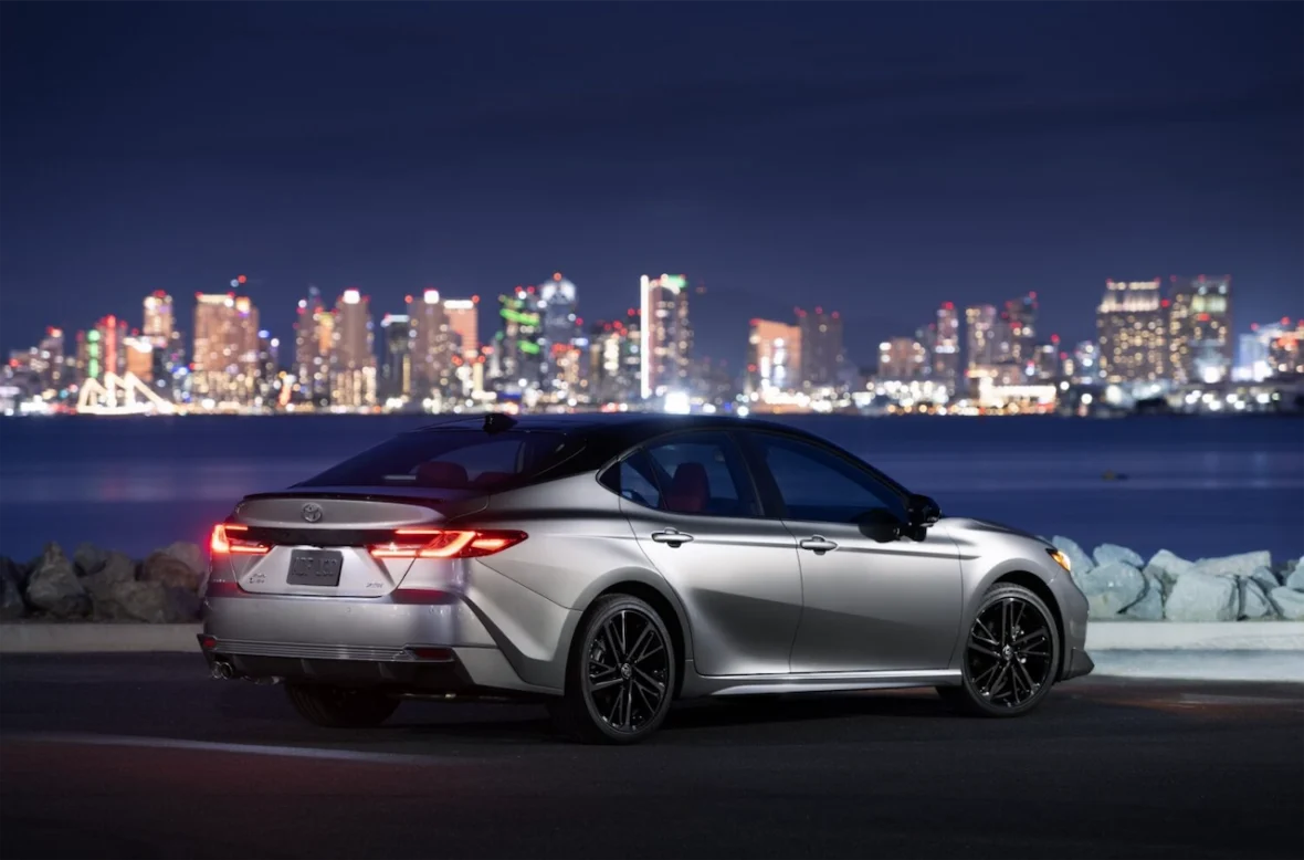 A silver sedan parked at night with a city skyline illuminated in the background.