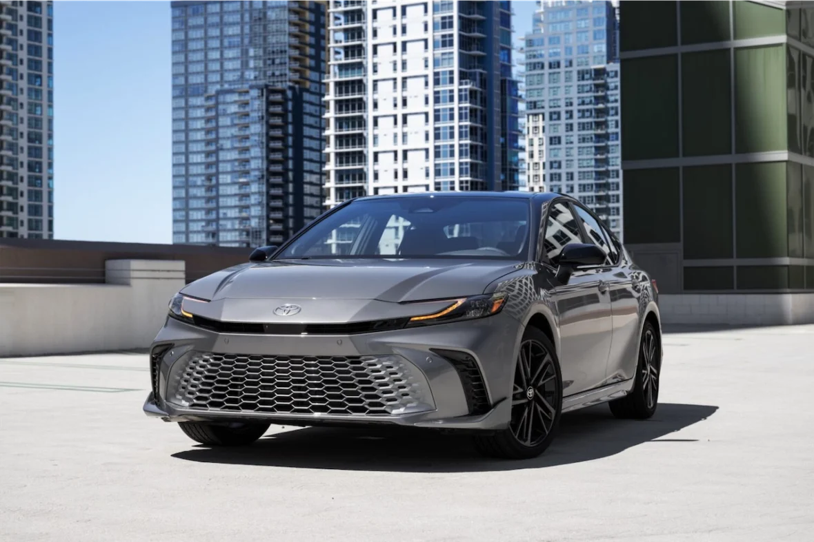 Front view of a silver Toyota car parked on a rooftop with modern skyscrapers in the background.