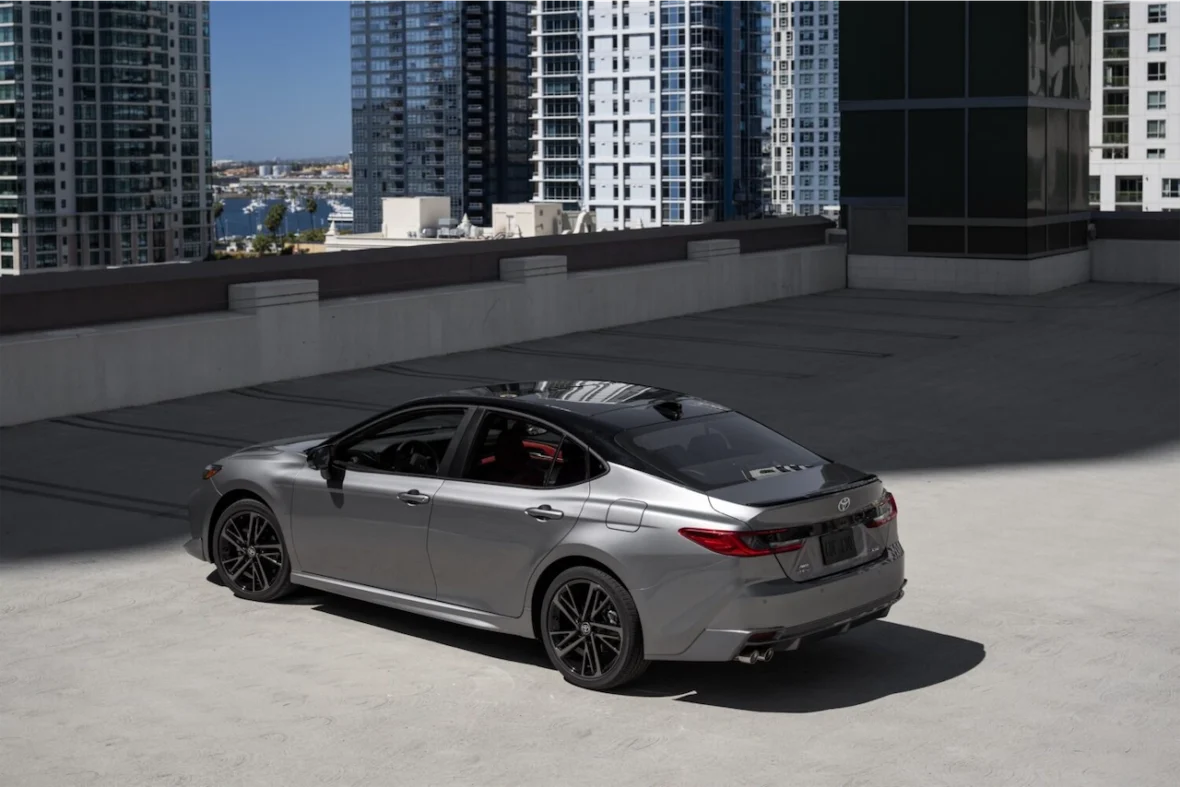 A silver sedan parked on a rooftop with modern high-rise buildings in the background.