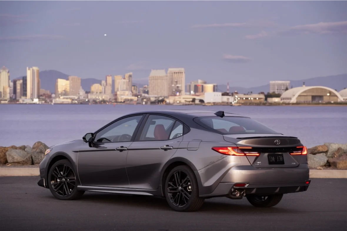 A sleek gray Toyota Camry parked by the waterfront, with the city skyline in the background during dusk.