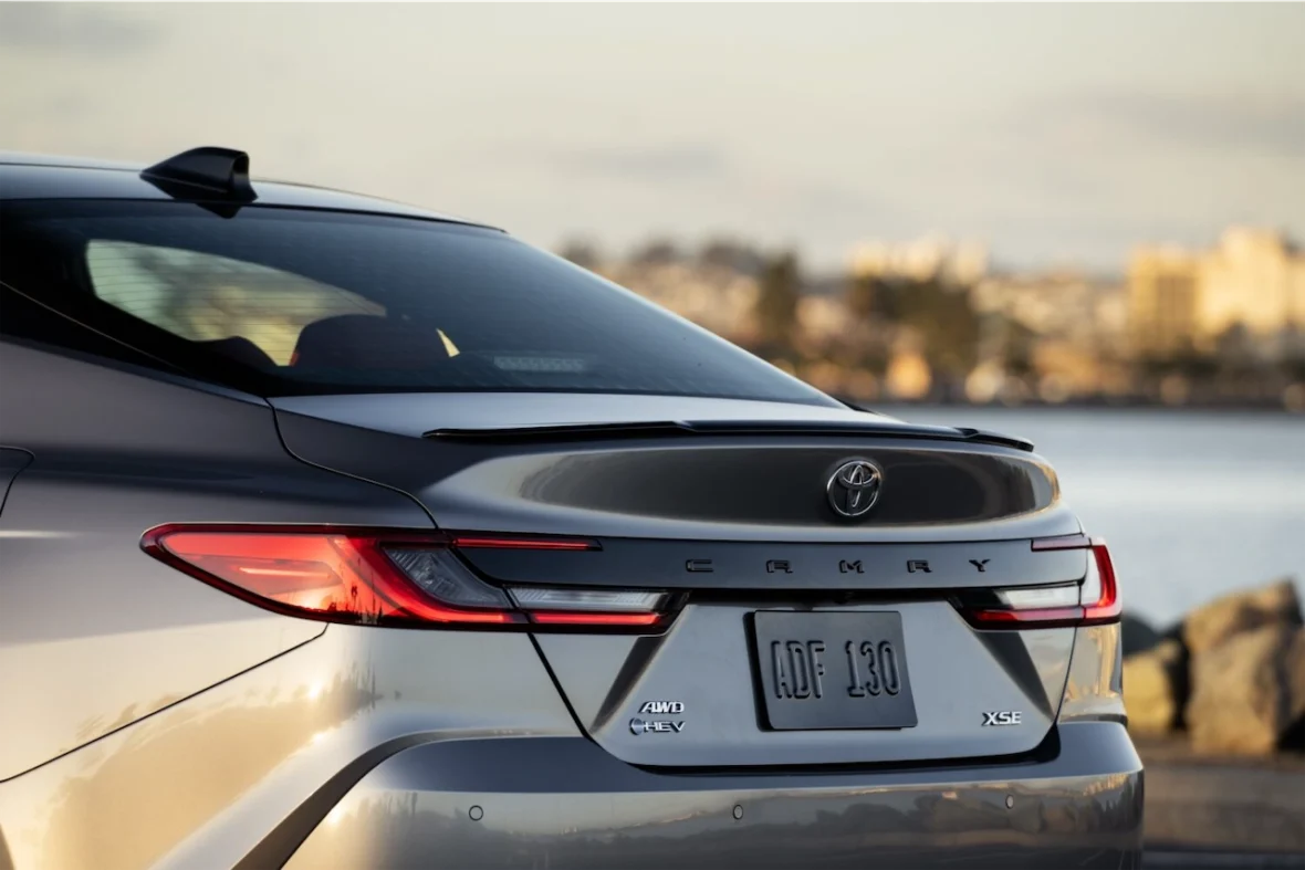 Close-up view of the rear of a grey Toyota Camry, showcasing the taillights, logo, and license plate near a waterfront.