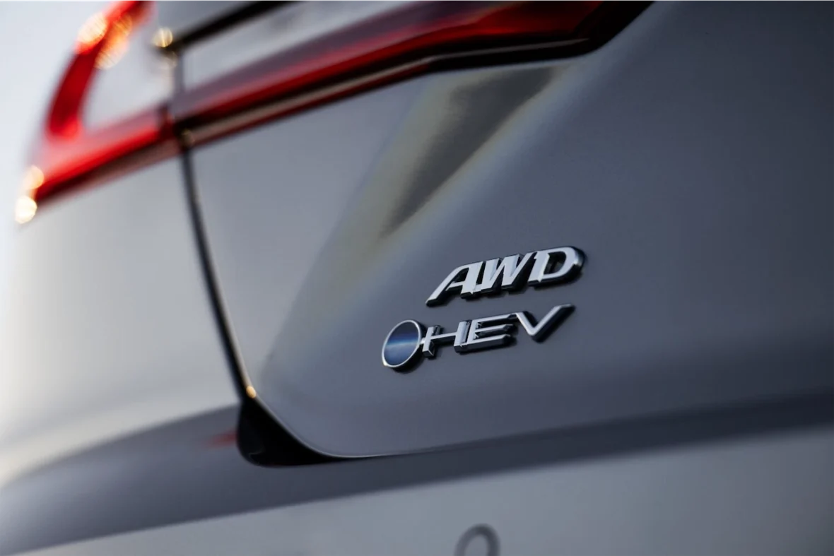 Close-up of a vehicle's rear badge displaying 'AWD' and 'HEV' on a grey surface.