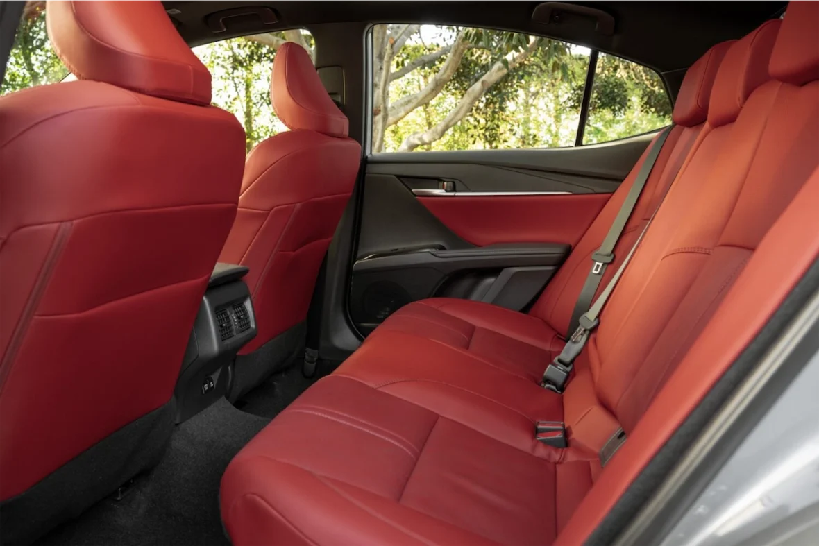 Interior view of a car's backseat featuring red leather upholstery, showcasing two seats with headrests and a view of the outside through the rear window.