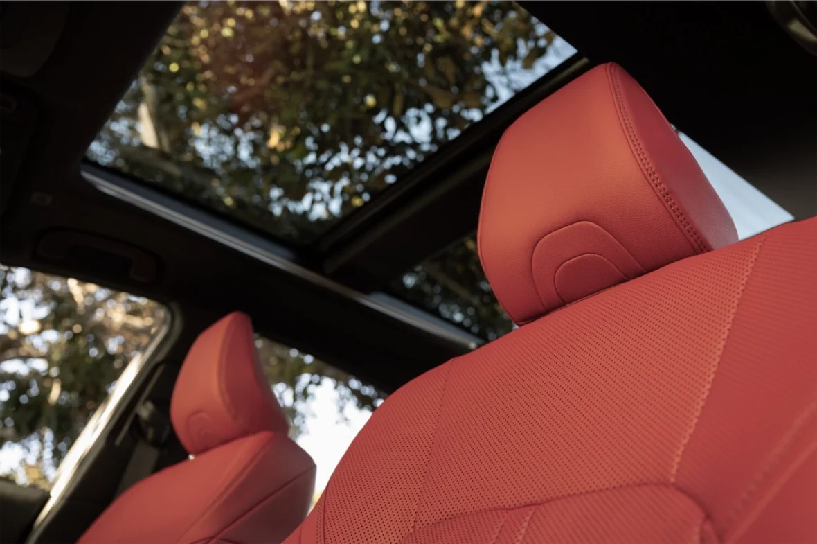 Interior view of a car showing red leather seats and a panoramic sunroof with trees in the background.