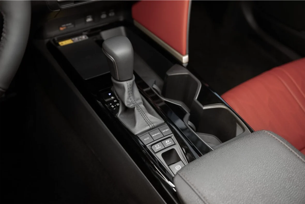 Close-up view of a car's center console featuring a gear shift, various driving mode buttons, and cup holders with red and black upholstery.