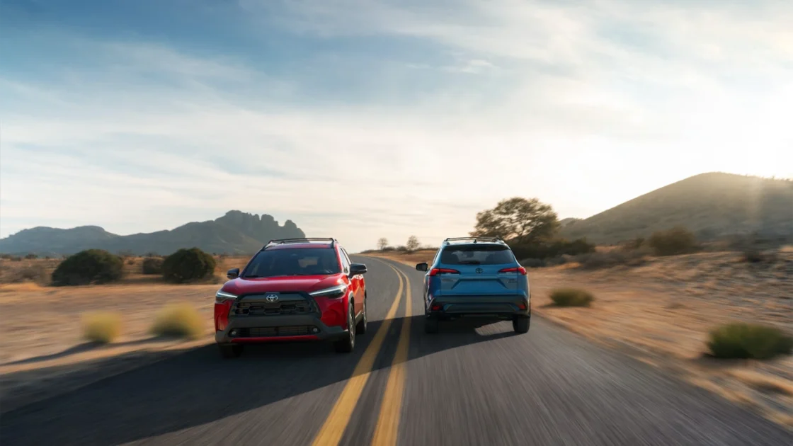 2027 Toyota Corolla Cross XLE in Soul Red Crystal and Hybrid XSE in Cavalry Blue driving on a desert road