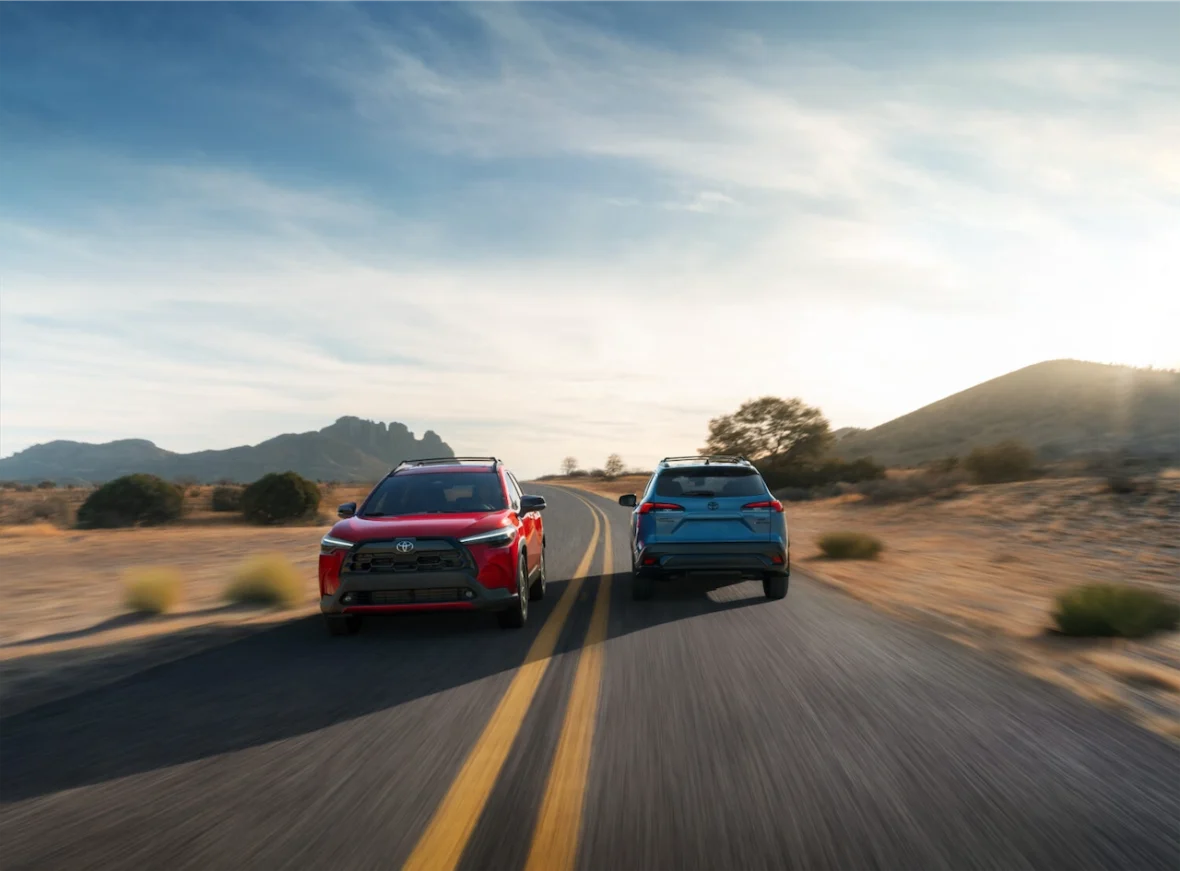 2027 Toyota Corolla Cross XLE in Soul Red Crystal and Hybrid XSE in Cavalry Blue driving on a desert road