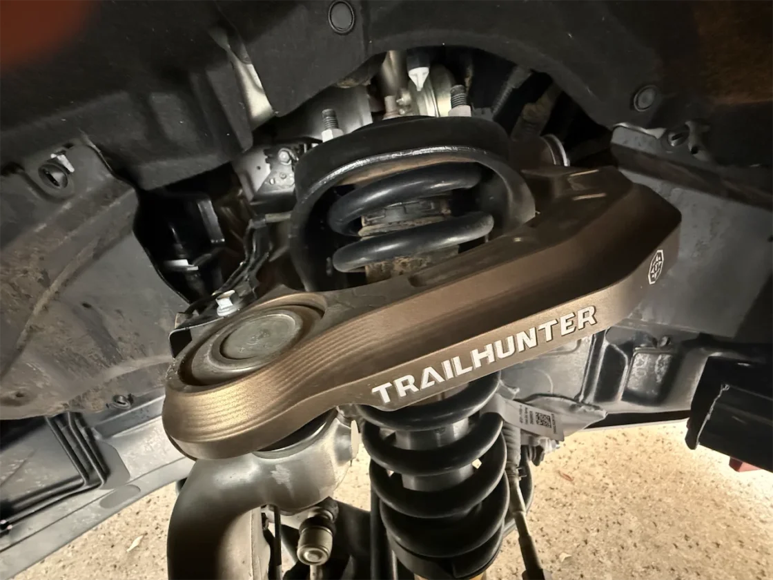 Close-up view of a vehicle's undercarriage showing a 'TRAILHUNTER' suspension component, including a coil spring and mounting bracket.
