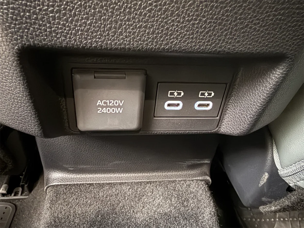 Close-up of a car interior power panel featuring a 120V AC outlet rated at 2400W and two USB-C charging ports.